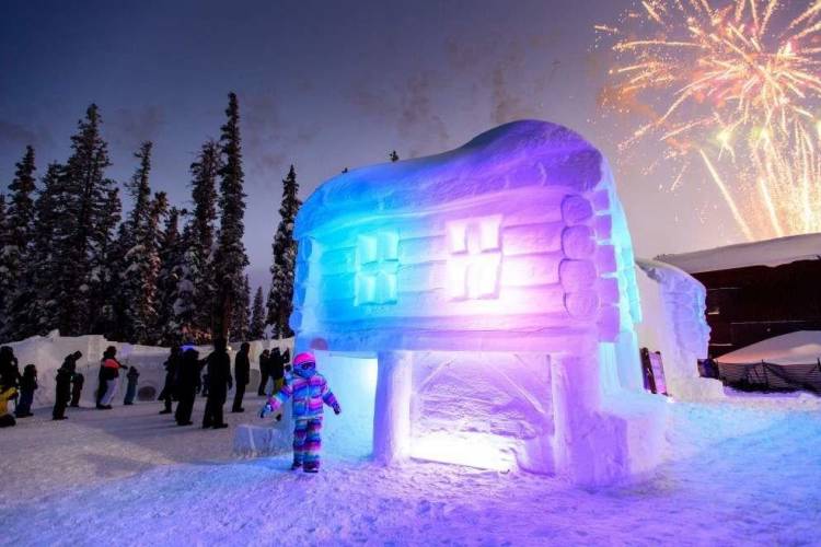 a large snowfort lit up with lights and a little girl standing there with fireworks in the background