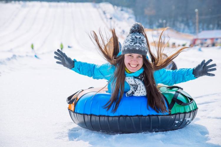 girl sliding down snow on a snow tube with her arms in the air